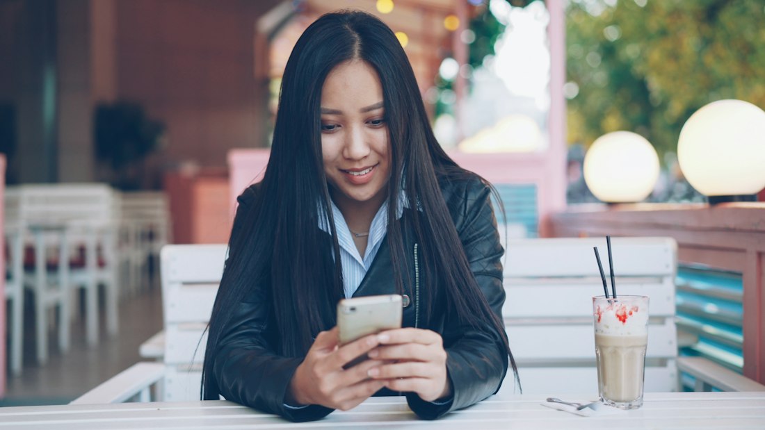 A young woman smiling at her phone in a café